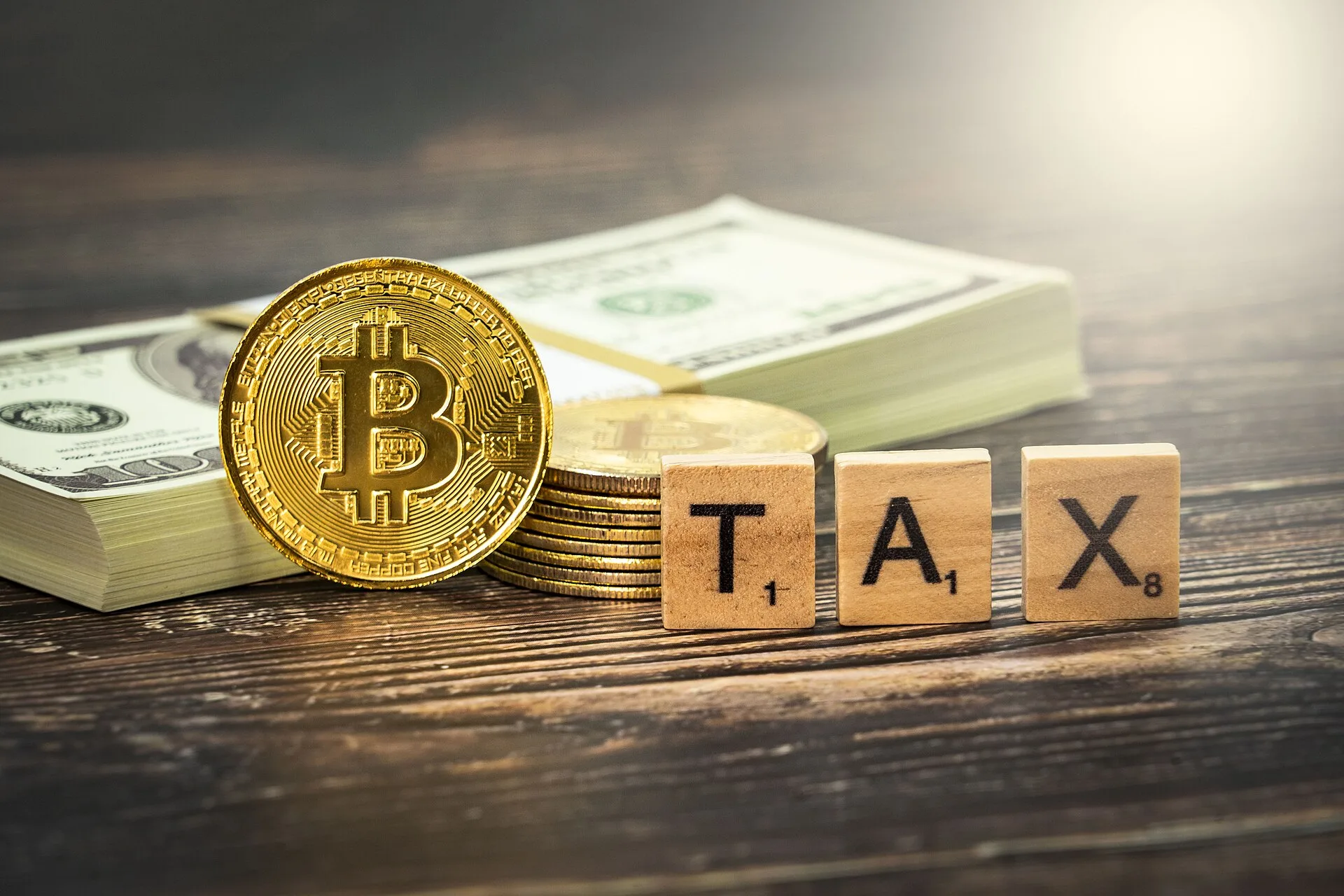 Crypto tax concept image that shows a Bitcoin cryptocurrency medallion alongside some cash and some Scrabble titles spelling out the word 'tax'. This image is available for you to use under the Attribution Creative Commons licence, though you must provide attribution in the form of a link to www.byb. IRS reporting for crypto, stablecoins, and payment-app income
